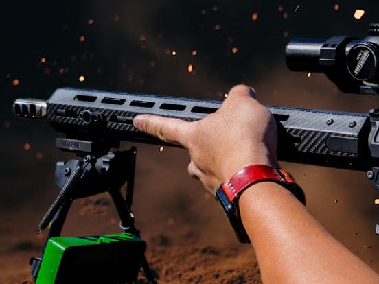 Person aiming a sleek rifle with a scope, surrounded by flying debris in an outdoor setting