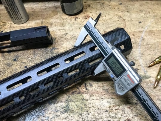 Measuring carbon fiber gun part with digital caliper on wooden workbench