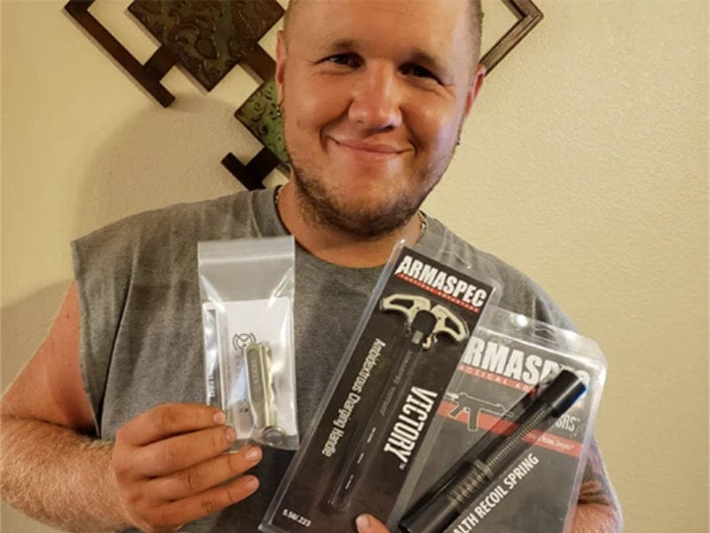 Happy man holding Armaspec products including a recoil spring and accessories