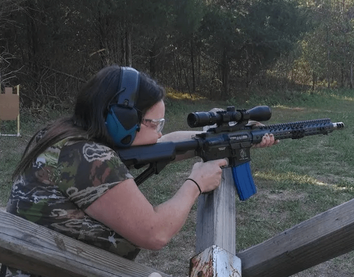 A person aiming a rifle on a shooting range, wearing protective gear and focused on the target